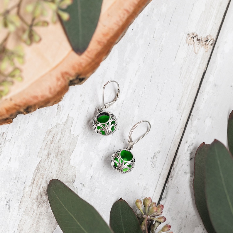 Op de afbeelding: Een paar zilveren oorbellen met groene glazen cabochons, ingelegd in een ingewikkeld filigraanontwerp.