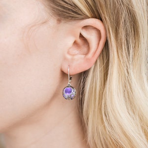 May include: Silver dangle earrings with a purple glass orb in a filigree design.