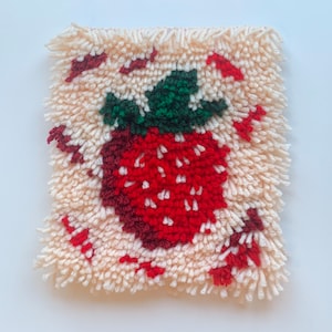 Könnte beinhalten: Nahaufnahme eines handgefertigten Teppichs mit einem roten und grünen Erdbeerdesign. Der Teppich ist aus flauschigem Garn gefertigt und hat einen weißen Hintergrund.