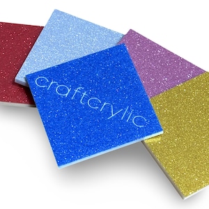 May include: Four sheets of glitter paper in blue, light blue, purple, and gold. The sheets are stacked on top of each other and the blue sheet has the word "craftylic" printed on it.