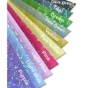 May include: A fan of colorful, iridescent craft paper sheets in shades of dark green, teal, green, pale green, yellow, pale yellow, pink, light pink, light blue, and purple. Each sheet has text labels. The paper has a holographic effect.