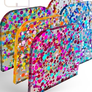 May include: A set of four clear acrylic squares with a confetti pattern. The squares are stacked on top of each other, with the largest square on the bottom and the smallest square on top. The confetti pattern is made up of small, colorful circles.