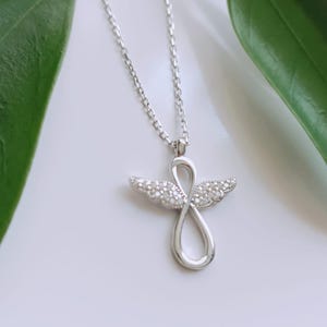 May include: A silver necklace with a pendant shaped like an infinity symbol with wings. The wings are decorated with small, clear stones.