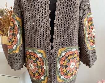 Puede incluir: Un cárdigan de ganchillo marrón con un diseño floral en las mangas y la parte delantera. El cárdigan tiene cuello en V y un corte holgado.