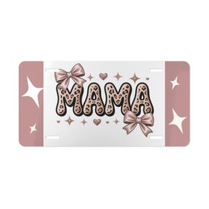 May include: A license plate with the word "MAMA" in a leopard print font, adorned with bows and hearts. The plate has a white center and pink edges with star and heart accents.