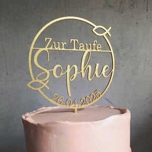 Könnte beinhalten: Goldener Tortendekor mit einem Kreis und dem Text "Zur Taufe Sophie 26.04.2025" und einem Fischsymbol.
