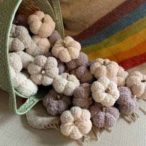 May include: A basket overflowing with crocheted pumpkins in shades of cream and brown. The pumpkins are arranged in a cascading pattern, creating a cosy and autumnal display.