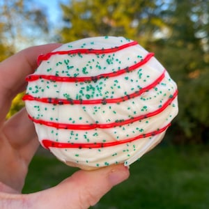 May include: A white chocolate covered cookie with red and green sprinkles. The cookie is decorated with red stripes and green sprinkles.