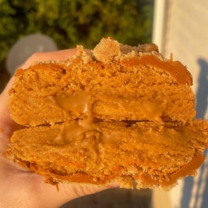 Peut inclure: Une pâtisserie coupée en deux, de couleur brun doré, avec une garniture crémeuse de couleur caramel. La pâtisserie a une surface texturée et est garnie d'une garniture friable brun clair. Le dessert est tenu dans une main.