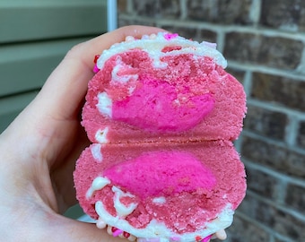 Puede incluir: Una galleta rosa y blanca con chispas, cortada por la mitad para mostrar el relleno rosa en el interior.