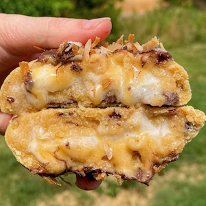 Peut inclure: Un cookie coupé en deux avec des pépites de chocolat, une couche de guimauve et un filet de caramel. Le cookie est recouvert de noix de coco râpée.