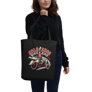 Puede incluir: Bolso tote negro con un gráfico de un caimán en bicicleta y el texto "KOLOSSOS BIKE ZOO". El caimán es rojo, blanco y negro. Las ruedas de la bicicleta son rojas. El bolso lo lleva una persona.