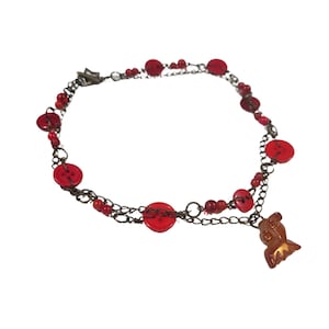 Può includere: Una collana di bottoni rossi e perline con un ciondolo marrone. La collana è composta da due catene con bottoni e perline rosse.