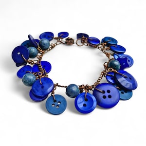 Può includere: Bracciale fatto a mano con bottoni e perline blu su una catena color rame. Il bracciale ha una chiusura a fermaglio. I bottoni sono di varie dimensioni e tonalità di blu.