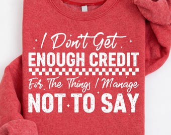 May include: Red sweatshirt with white text: "I Don't Get Enough Credit For The Things I Manage NOT TO SAY." The text is in a mix of fonts. The sweatshirt is folded with the sleeves visible.