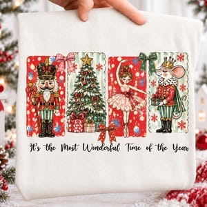 May include: A white t-shirt featuring a graphic print of a nutcracker, a decorated Christmas tree, a ballerina, and a mouse dressed as a prince. The text "It's the Most Wonderful Time of the Year" is printed in black script below the colorful illustrations.