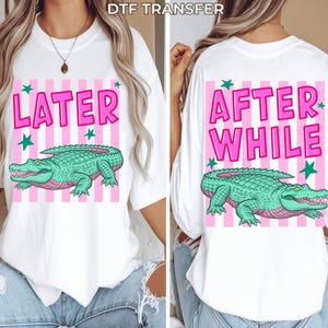 May include: White t-shirt with a front graphic that says "LATER" in pink, with a green alligator illustration. The back of the shirt says "AFTER WHILE" in pink, with the same alligator design. Pink and white striped background.