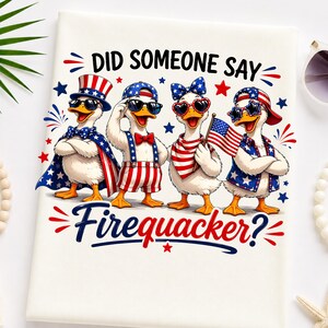 May include: A white t-shirt featuring a graphic of four ducks dressed in patriotic American-themed clothing, including top hats, bow ties, and star-spangled accessories. The text reads DID SOMEONE SAY Firequacker? in black and red lettering.
