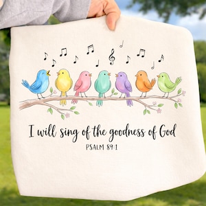 May include: A cream-colored fabric item featuring a graphic of seven colorful birds perched on a brown branch with musical notes above them. The text reads, I will sing of the goodness of God, followed by the scripture reference, PSALM 89:1.
