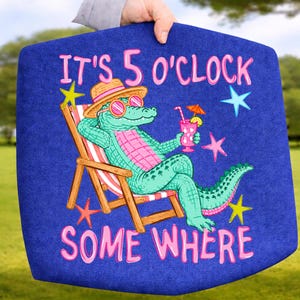 May include: A blue tote bag featuring a cartoon alligator in sunglasses and a straw hat, relaxing in a beach chair with a cocktail. The text "IT'S 5 O'CLOCK SOMEWHERE" is written in pink.