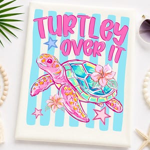 May include: A cream-colored t-shirt with a colorful graphic of a sea turtle and the words "TURTLEY OVER IT" in pink. The turtle is pink, blue, and yellow, with hibiscus flowers and star accents. Blue vertical stripes are in the background.