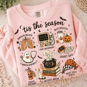 May include: A light pink sweatshirt featuring the text 'tis the season' and various Halloween-themed medical illustrations including a pumpkin lung, a heart monitor, a jack-o'-lantern cup, a ghost with a stethoscope, and a cauldron on books.
