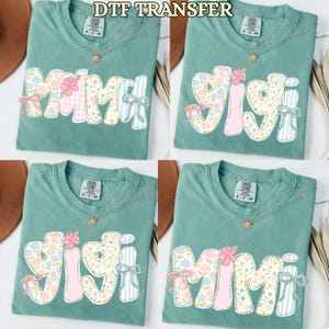 May include: Four sage green t-shirts with floral and striped text designs that read "MAMA", "GIGI", and "MIMI". Each shirt has a gold necklace. The text "DTF TRANSFER" is at the top.