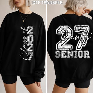 May include: A black long-sleeve sweatshirt featuring white graphic text. The front displays vertical text reading Class of 2027. The back features a large distressed 27 with the word twenty in script and the word SENIOR printed below in block letters.
