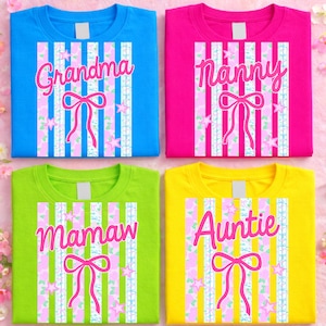 May include: Four colorful t-shirts: blue, pink, green, and yellow. Each shirt features a vertical striped design with a bow and stars. The shirts have the words "Grandma", "Nanny", "Mamaw", and "Auntie" in pink script.