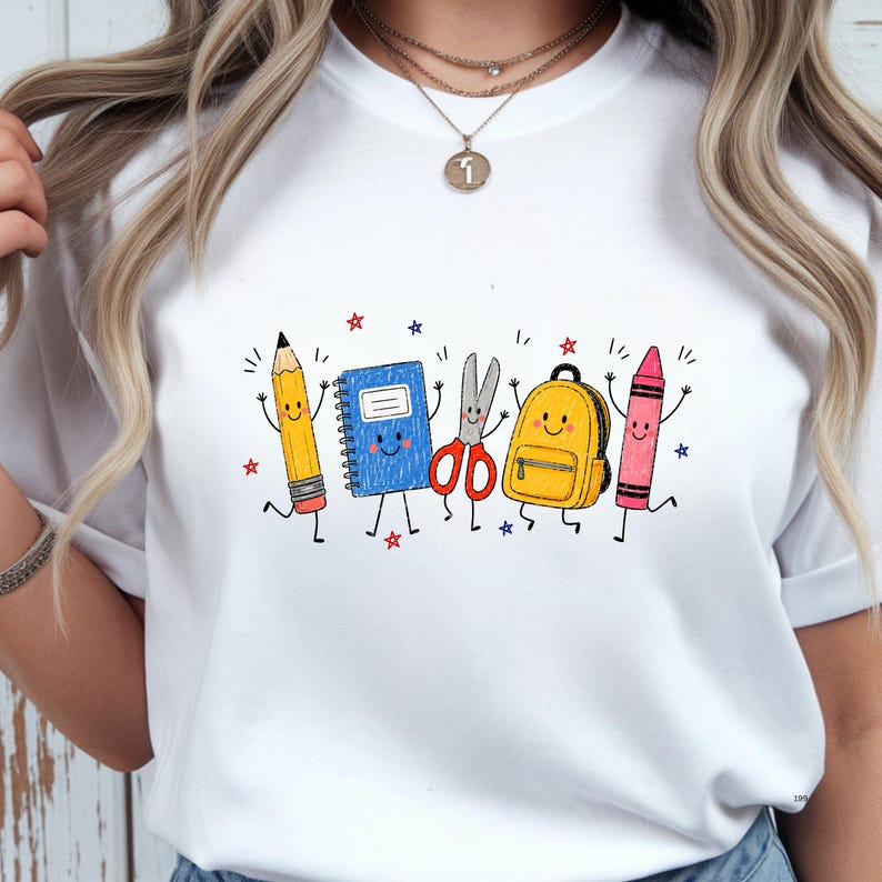 May include: A white t-shirt featuring a colorful graphic print of anthropomorphic school supplies including a yellow pencil, a blue spiral notebook, red scissors, a yellow backpack, and a pink crayon, all accented with small red and blue stars.