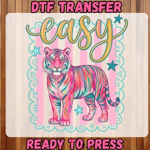 May include: A colorful tiger design with the word "easy" in a script font. The tiger is pink, blue, and green, with a pink and white striped background. The text "DTF TRANSFER" and "READY TO PRESS" are also included.