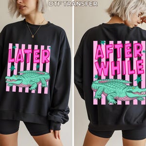 May include: Black sweatshirt with a pink and white striped design. The front features the word "LATER" above a green alligator illustration. The back of the sweatshirt has the words "AFTER WHILE" above the same alligator design.