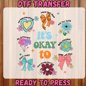May include: A DTF transfer design with the text "it's OKAY to" in a retro font, surrounded by colorful illustrations of flowers, bows, and phrases like "Have bad days" and "Make mistakes." The words "DTF TRANSFER" and "READY TO PRESS" are also present.