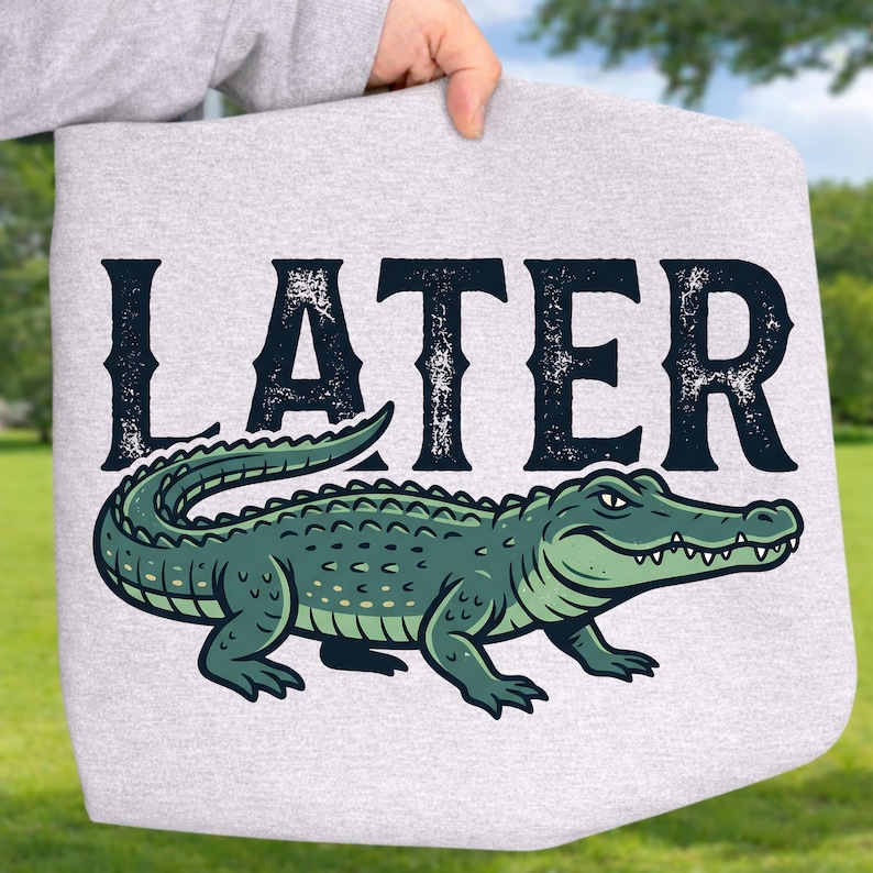 May include: A light gray tote bag featuring a green alligator illustration with the word "LATER" in distressed black lettering. The alligator is detailed with various shades of green and white accents.