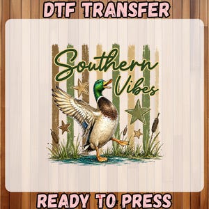 May include: DTF transfer featuring a watercolor illustration of a duck with outstretched wings, the words "Southern Vibes" in a script font, and the text "READY TO PRESS". The design includes stars and cattails.