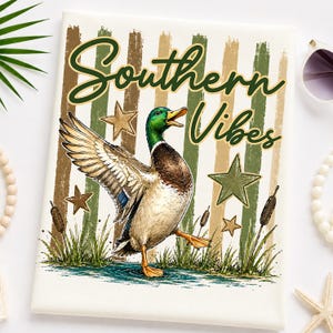 May include: A cream-colored decorative pillow featuring a mallard duck illustration with the text "Southern Vibes." The design includes green, brown, and tan stripes, stars, and cattails. The duck is depicted with its wing outstretched, walking in water.