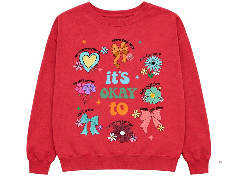 May include: Red sweatshirt with the phrase "it's OKAY to" and various positive affirmations and illustrations, including flowers, bows, and a heart. The sweatshirt has a crew neck and long sleeves.