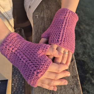 Puede incluir: Un par de guantes sin dedos de color morado hechos de hilo de ganchillo. Los guantes se muestran en las manos de una persona.