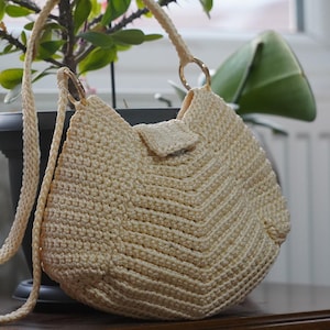 May include: A crocheted beige handbag with a long strap and a gold clasp. The bag is made of a woven material and has a chevron pattern.