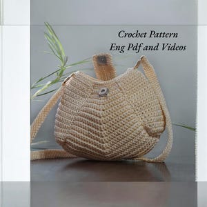 May include: A crocheted beige shoulder bag with a button closure and a long strap. Crochet Pattern Eng Pdf and Videos.