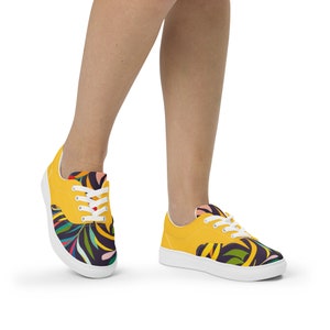 May include: A pair of yellow canvas low-top trainers with white laces and a colourful floral pattern on the back half of the shoe.