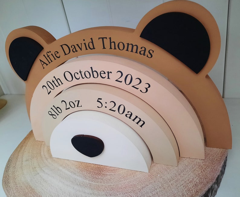 May include: A wooden bear-shaped keepsake with the name "Alfie David Thomas" and birth details: October 20th, 2023, 8lb 2oz, and 5:20am. The bear has tan, black, and white accents, and sits on a wooden base.