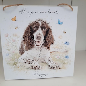 以下が含まれることがあります： 茶色と白の犬の水彩画が描かれた正方形の木製サイン。花と蝶に囲まれています。「Always in our hearts」の文字が犬の上に、名前の「Poppy」が下にあります。