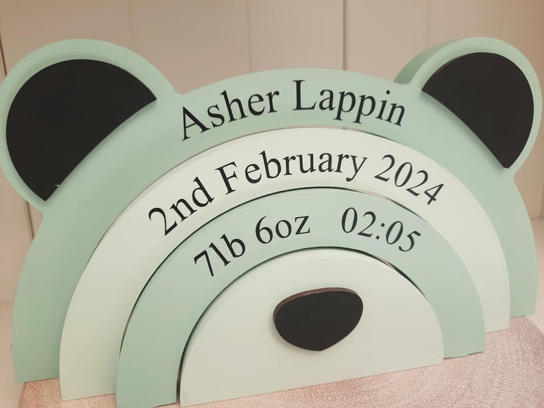 May include: A layered wooden bear-shaped sign in pastel green and white, with black accents. The sign displays the name "Asher Lappin", birthdate, weight (7lb 6oz), and time (02:05) in black text, perfect for a nursery or baby's room.