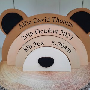 May include: A wooden bear-shaped keepsake with the name "Alfie David Thomas" and birth details. The bear has tan, black, and white elements, with the birth date, weight (8lb 2oz), and time (5:20am) displayed on layered arches.