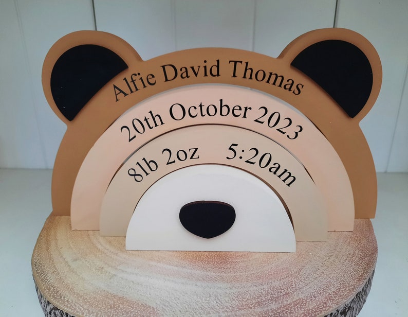 May include: A wooden bear-shaped keepsake with the name "Alfie David Thomas" and birth details. The bear has tan, black, and white elements, with the birth date, weight (8lb 2oz), and time (5:20am) displayed on layered arches.