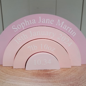 Könnte beinhalten: Ein rosafarbener Holzregenbogenbogen mit dem Namen "Sophia Jane Martin", dem Datum "18. Januar 2024", dem Gewicht "7lb 10oz" und der Länge "10.34" eingraviert.