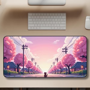 May include: A rectangular desk mat featuring a vibrant illustration of a street lined with pink cherry blossom trees under a sunset sky. A black cat is in the center of the road. The mat is surrounded by a keyboard, mouse, and monitor.