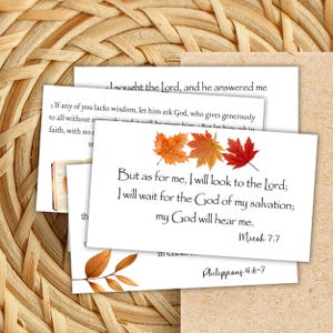 May include: A stack of white cards with Bible verses and autumn leaf illustrations. The cards feature text from Micah 7:7 and Philippians 4:6-7. The background is a woven, natural-toned surface.