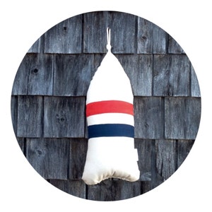 May include: A white buoy-shaped pillow with red, white, and blue stripes hanging on a wooden wall.